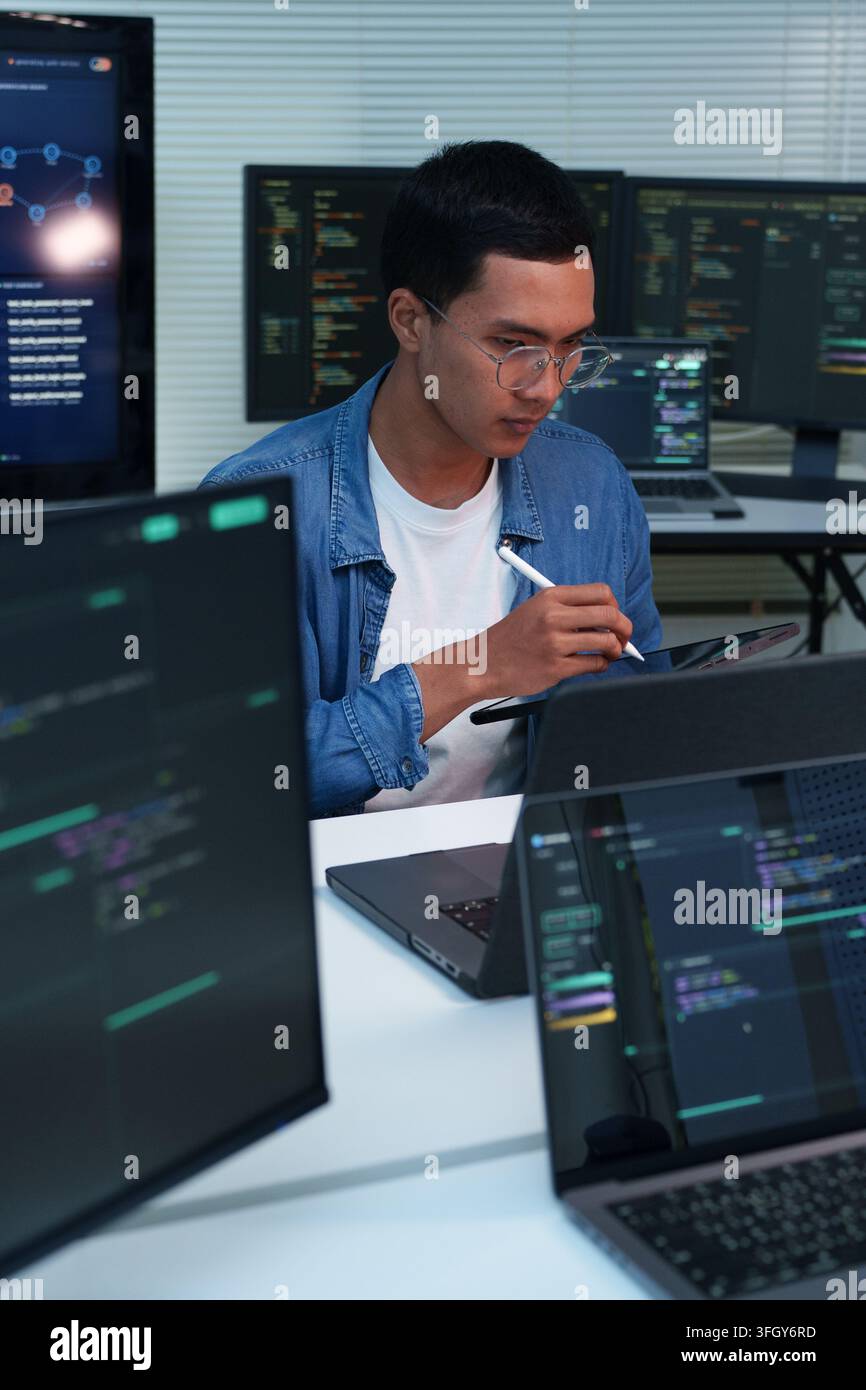 Focused programmer reviewing code and developing digital software, artificial intelligence, and cybersecurity solutions across multiple computer scree Stock Photo