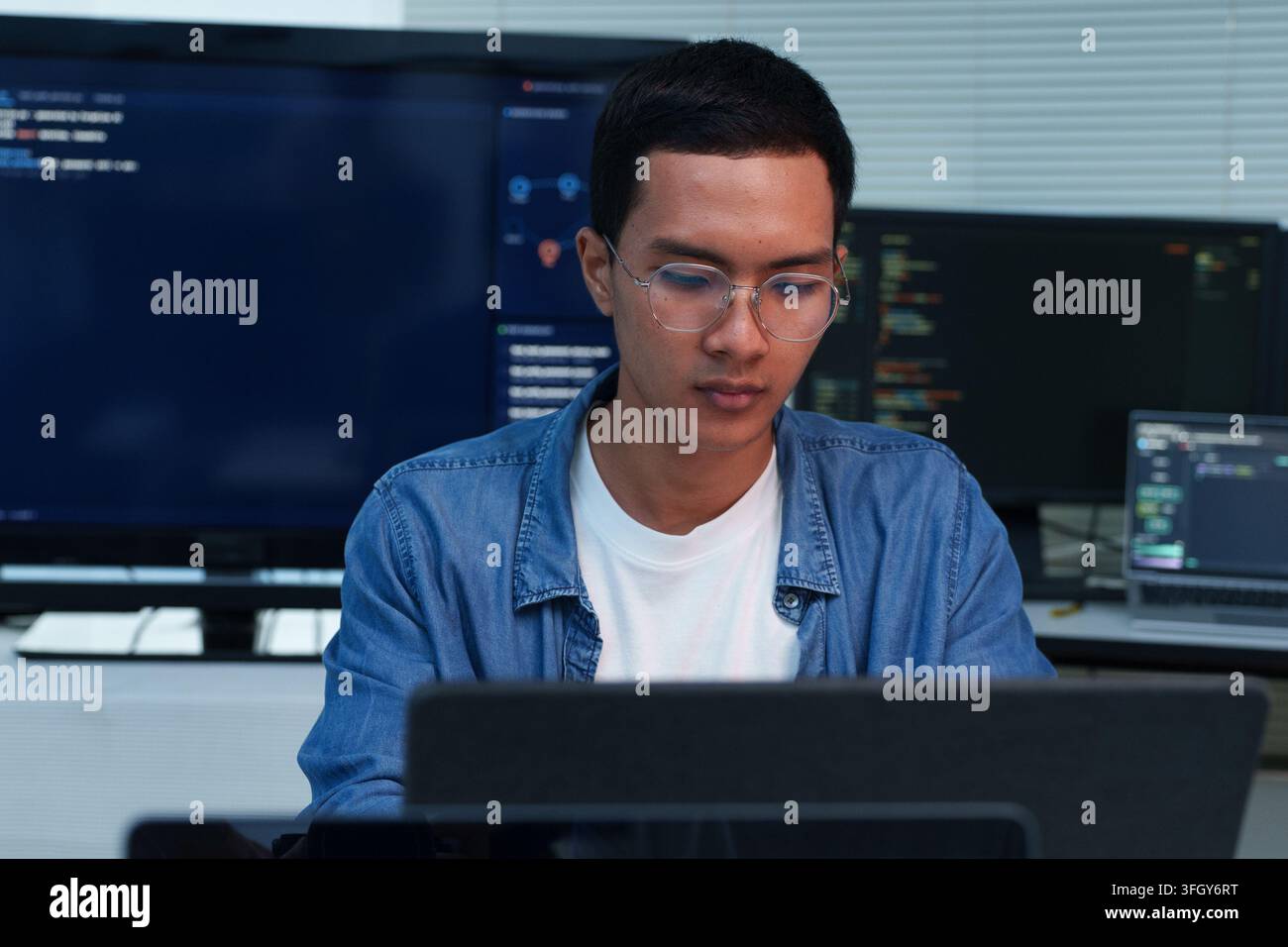 A focused young programmer works on a laptop, writing code and developing digital software solutions with expertise in programming, technology, and ar Stock Photo