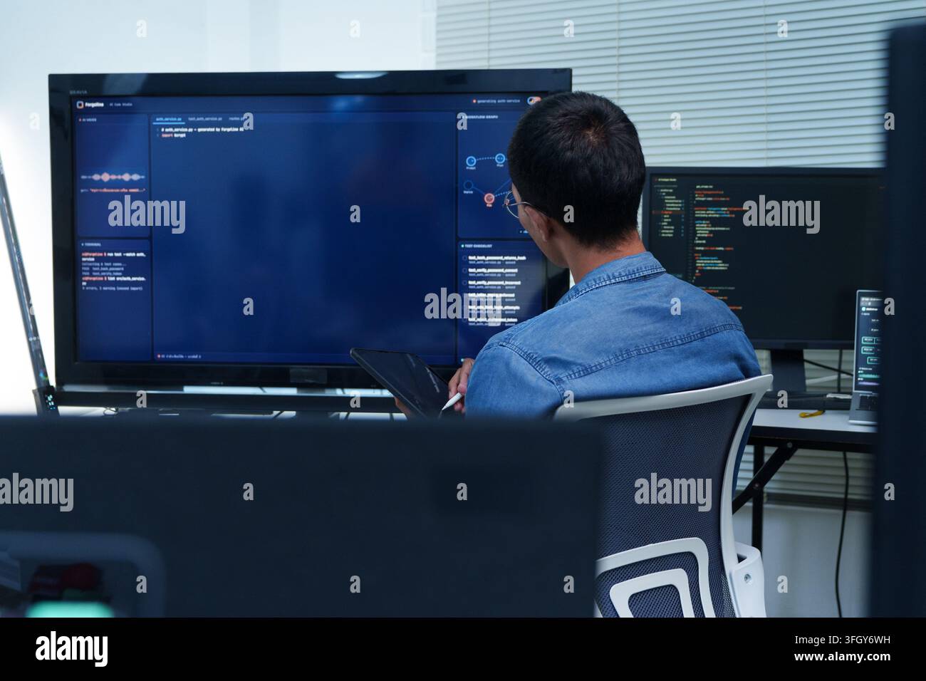 A software developer works with digital code, programming tools, and artificial intelligence technology on multiple computer screens. Stock Photo
