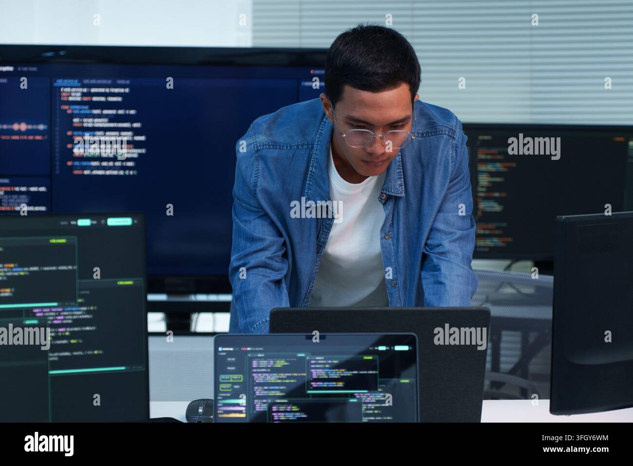 Focused programmer working on software development and writing code across multiple screens, representing digital technology, cybersecurity, artificia Stock Photo