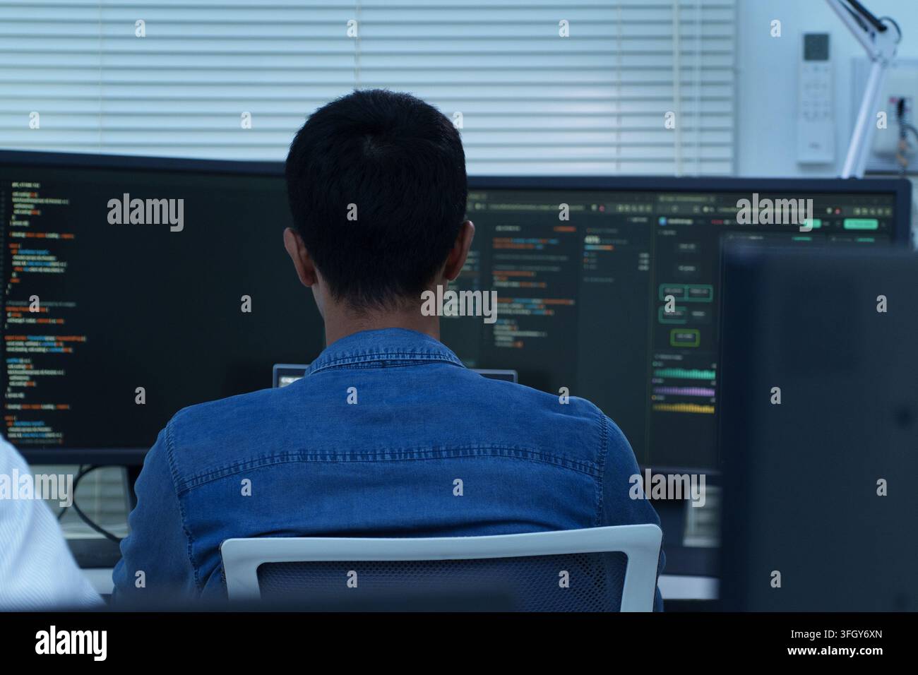 Back view of a programmer writing software code and developing artificial intelligence technology for digital and cyberspace applications. Stock Photo
