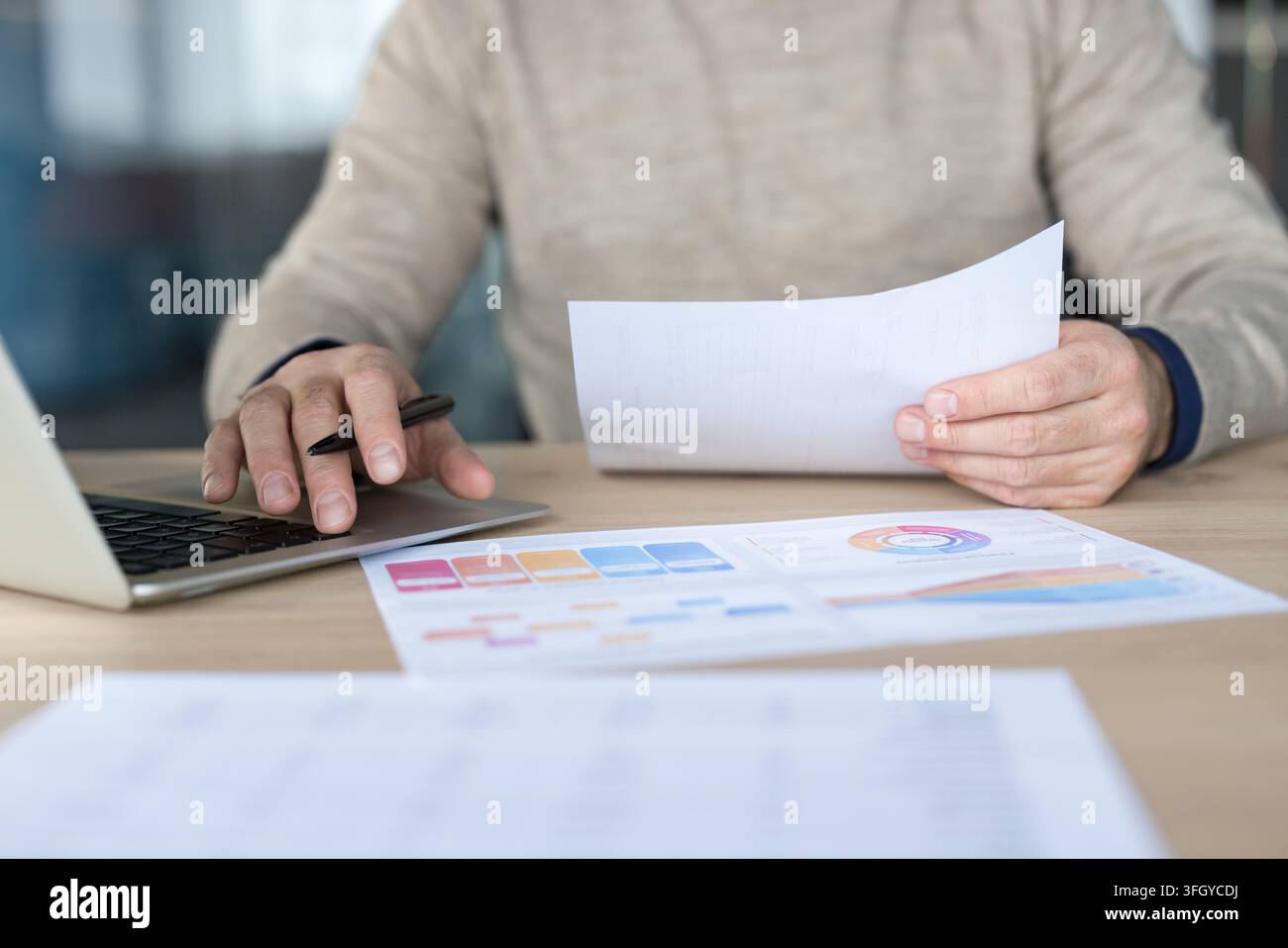 Businessman Working On Financial Analysis With Laptop And Documents At Desk In Office. Professional Manager Reading Paper Report And Using Computer For Strategic Planning In Corporate Workplace. Stock Photo