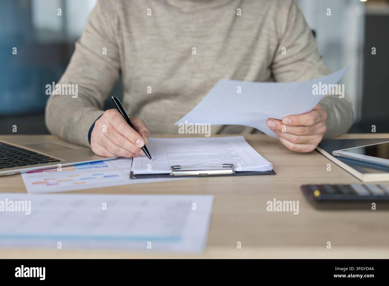 Businessman Writing On Documents At Desk In Office For Financial Analysis And Planning. Professional Manager Working With Laptop And Paperwork In Corporate Office Setting. Stock Photo