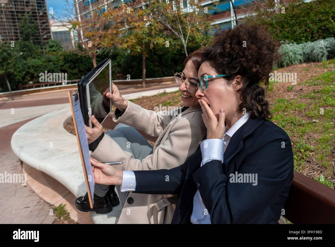 Businesswomen collaborating outdoors receiving surprising news on tablet Stock Photo