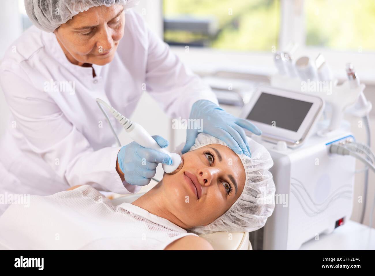 Female cosmetologist doing anti-aging face hardware therapy procedure ...