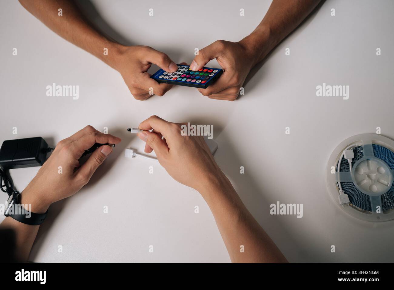 Two technicians connecting RGB led strip lights using remote control and controller, adjusting backlight settings for customized illumination. Stock Photo
