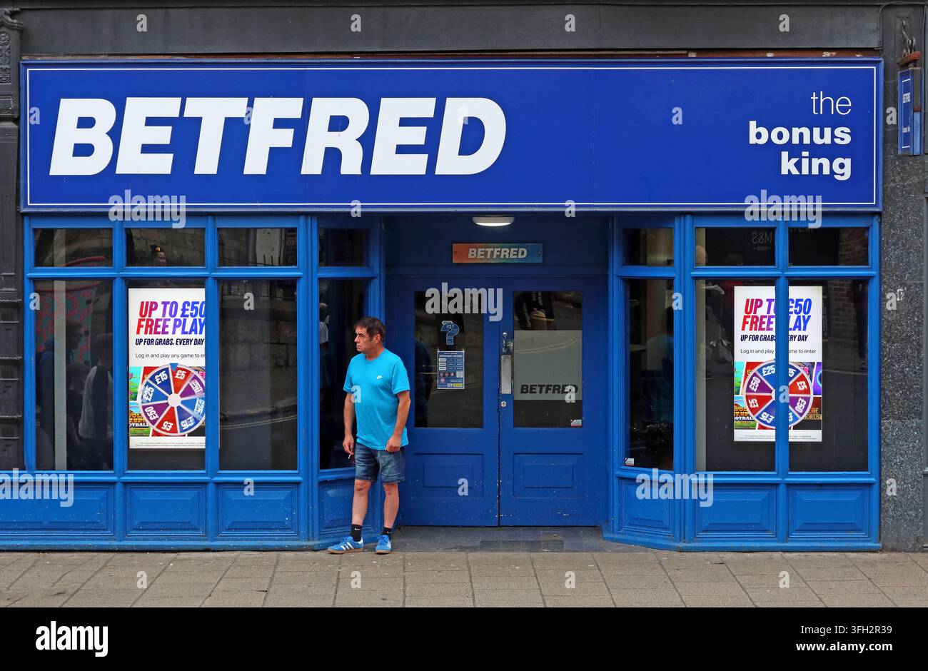 Customer or passer-by resting outside a Betfred betting shop in York, with gambling promotions displayed across the blue shopfront. Stock Photo