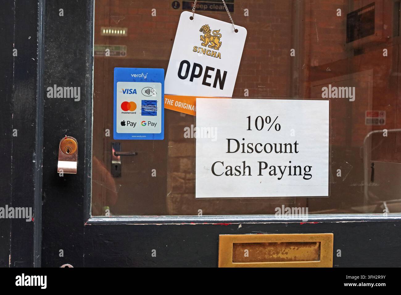 Shop window sign offering a 10% discount for customers paying by cash, alongside card-payment stickers and an open sign. Stock Photo