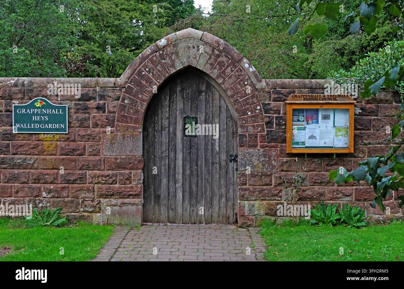 Stone-arched entrance to Grappenhall Heys Walled Garden in Warrington, with a timber door and visitor information beside the gateway. Stock Photo