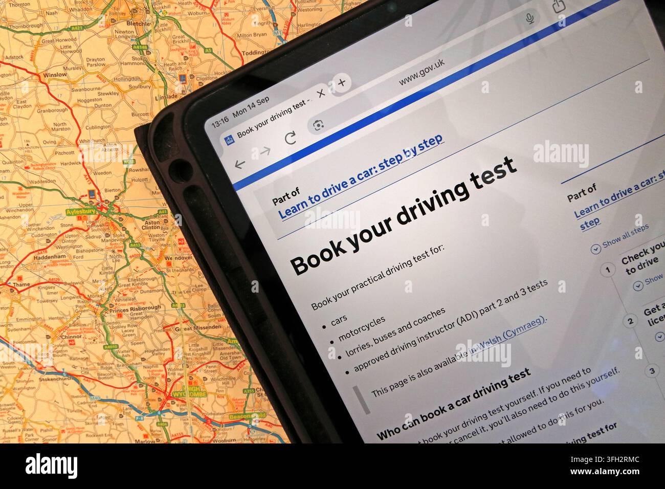 GOV.UK 'Book your driving test' service on an iPad over a road map, illustrating online practical-test booking in England. Stock Photo