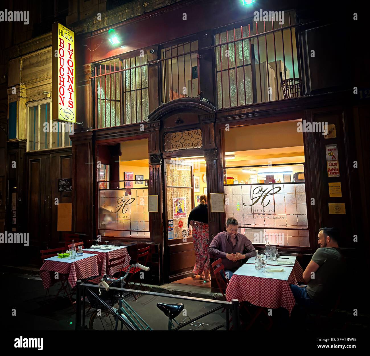 Chez Hugon, a traditional Lyonnais bouchon at 12 Rue Pizay in Lyon, with diners visible through the warmly lit restaurant frontage. Stock Photo