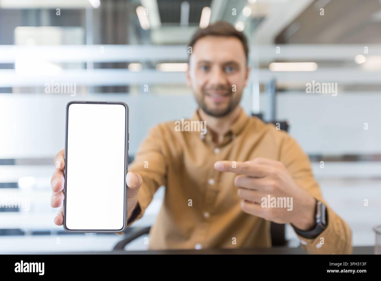 Mobile app promotion and digital marketing concept, man pointing at blank smartphone screen for mockup in office. Professional business communication and technology strategy. Stock Photo