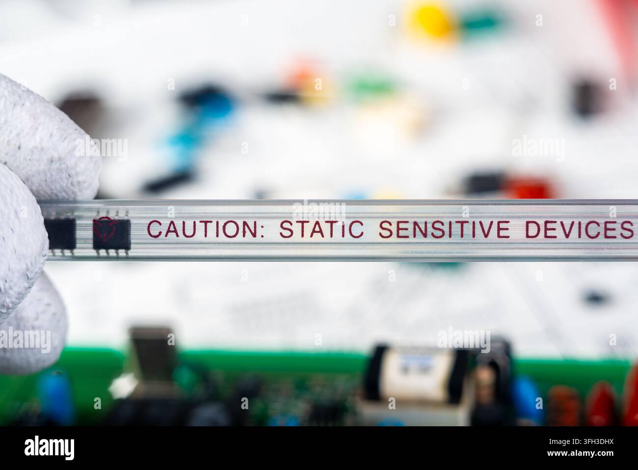 A person holds a caution sign about static sensitive devices while working with electronic components on a table filled with tools and parts. Stock Photo