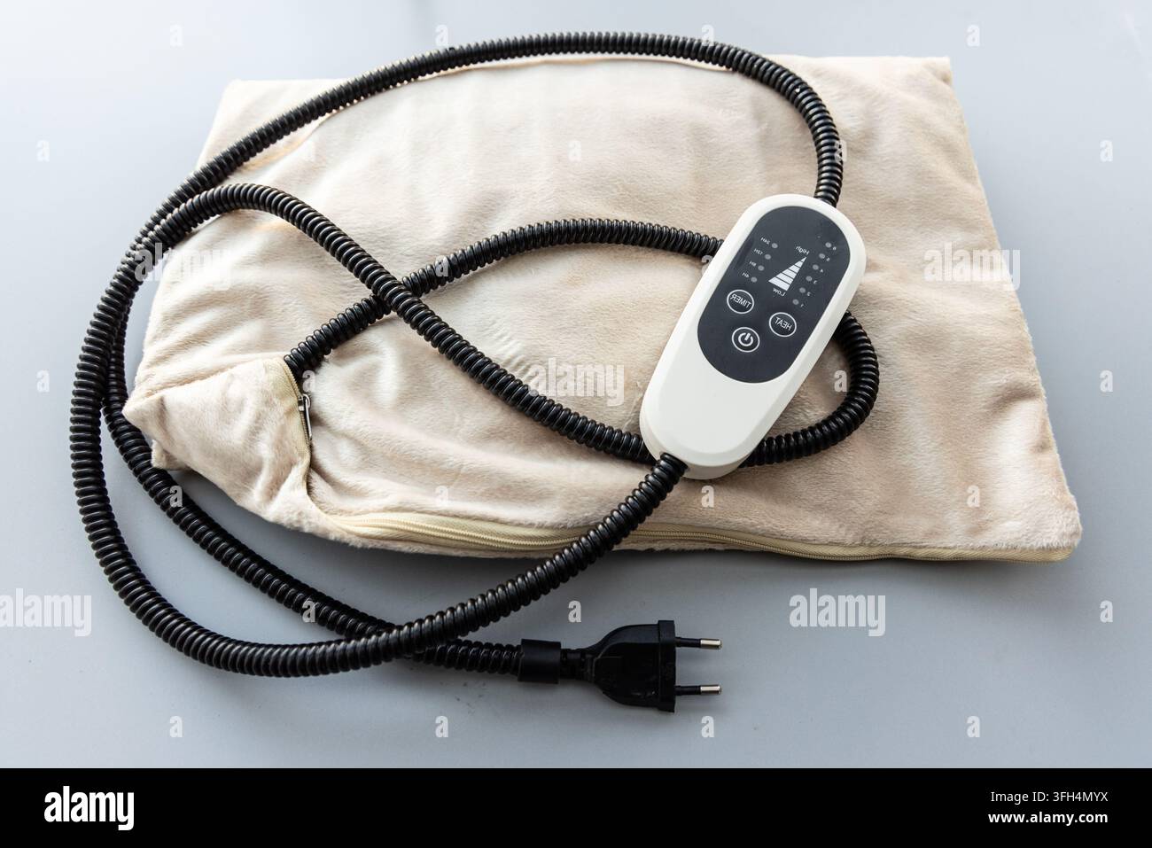 A beige electric heating pad with a controller on a grey background Stock Photo