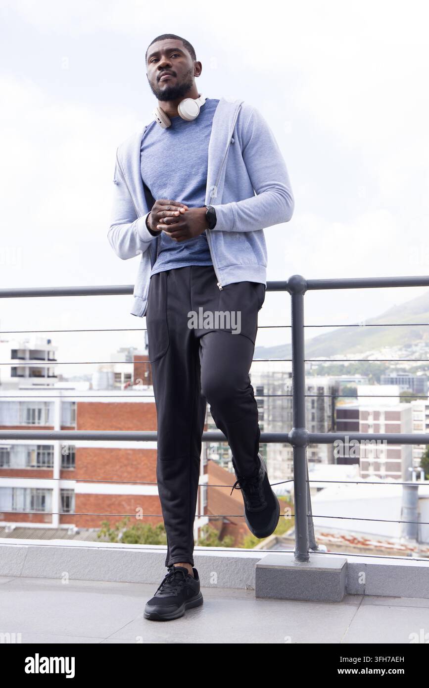 Man standing on rooftop terrace leaning on railing with headphones and smartwatch Stock Photo