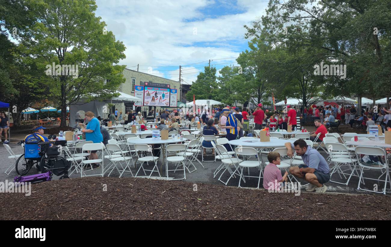 Crowds gather around tables and food vendors in the outdoor dining area of a community charity fair, with families - Smartphone Captured Stock Image