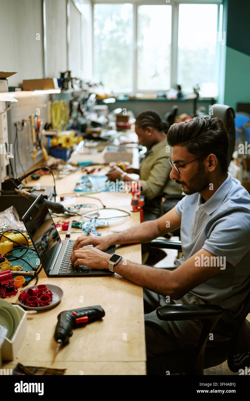 Indian Engineer Typing on Laptop in Hardware Workshop Stock Photo