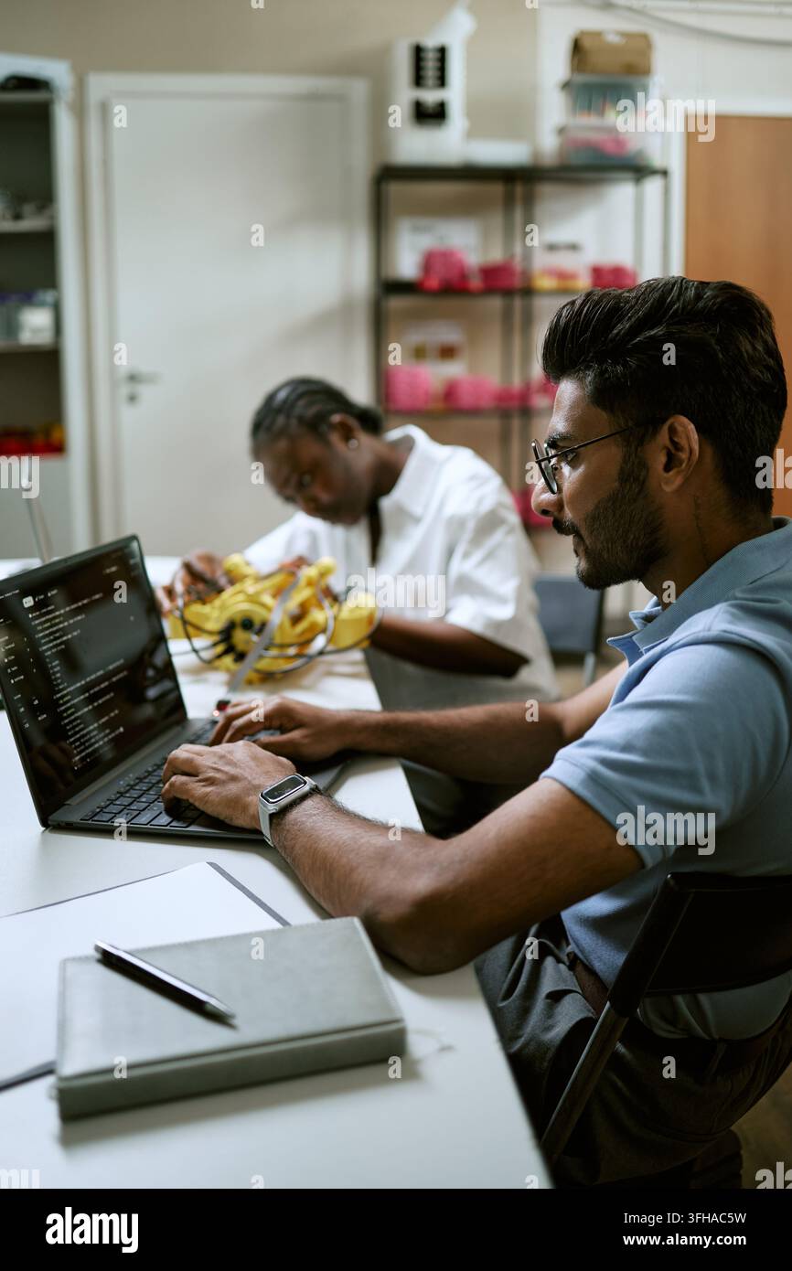 Indian Man Coding on Laptop in Robotics Technology Laboratory Stock Photo