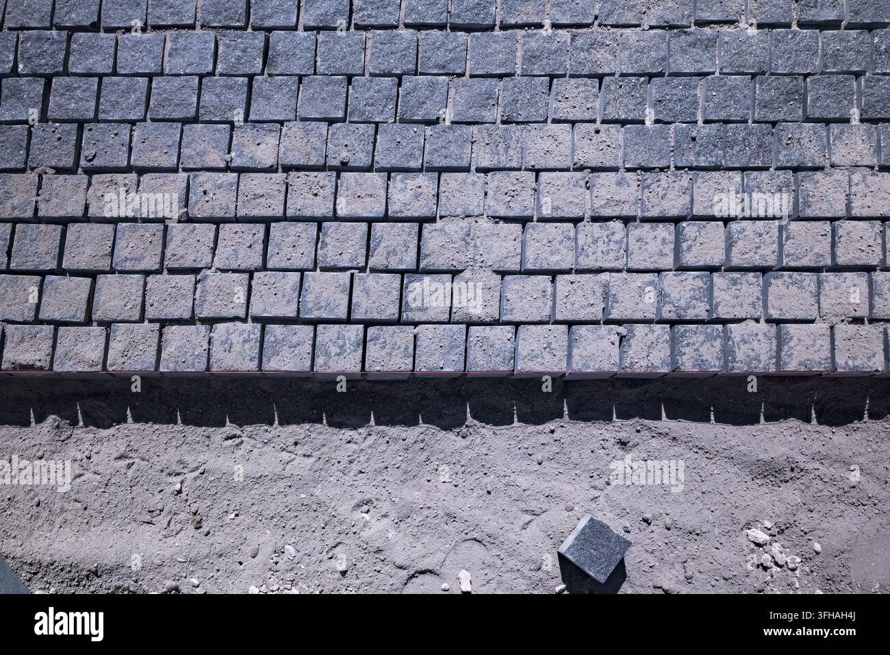 High angle view of granite cobblestone blocks being laid on a sand foundation during sidewalk construction outdoors. Stock Photo