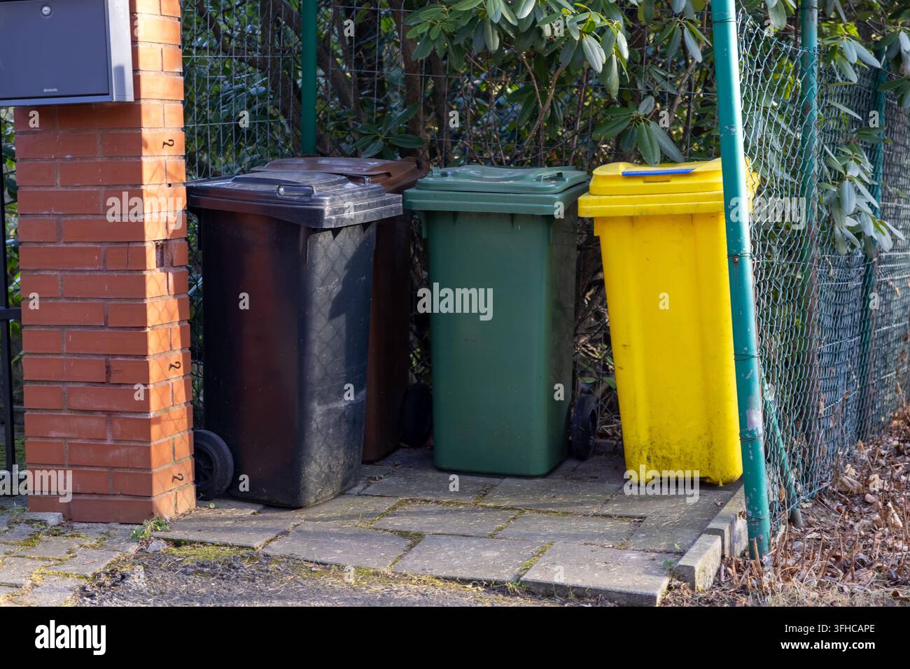 Black, green, and yellow household waste bins are neatly arranged on outdoor pavement by a brick pillar, highlighting effective waste sorting for urba Stock Photo