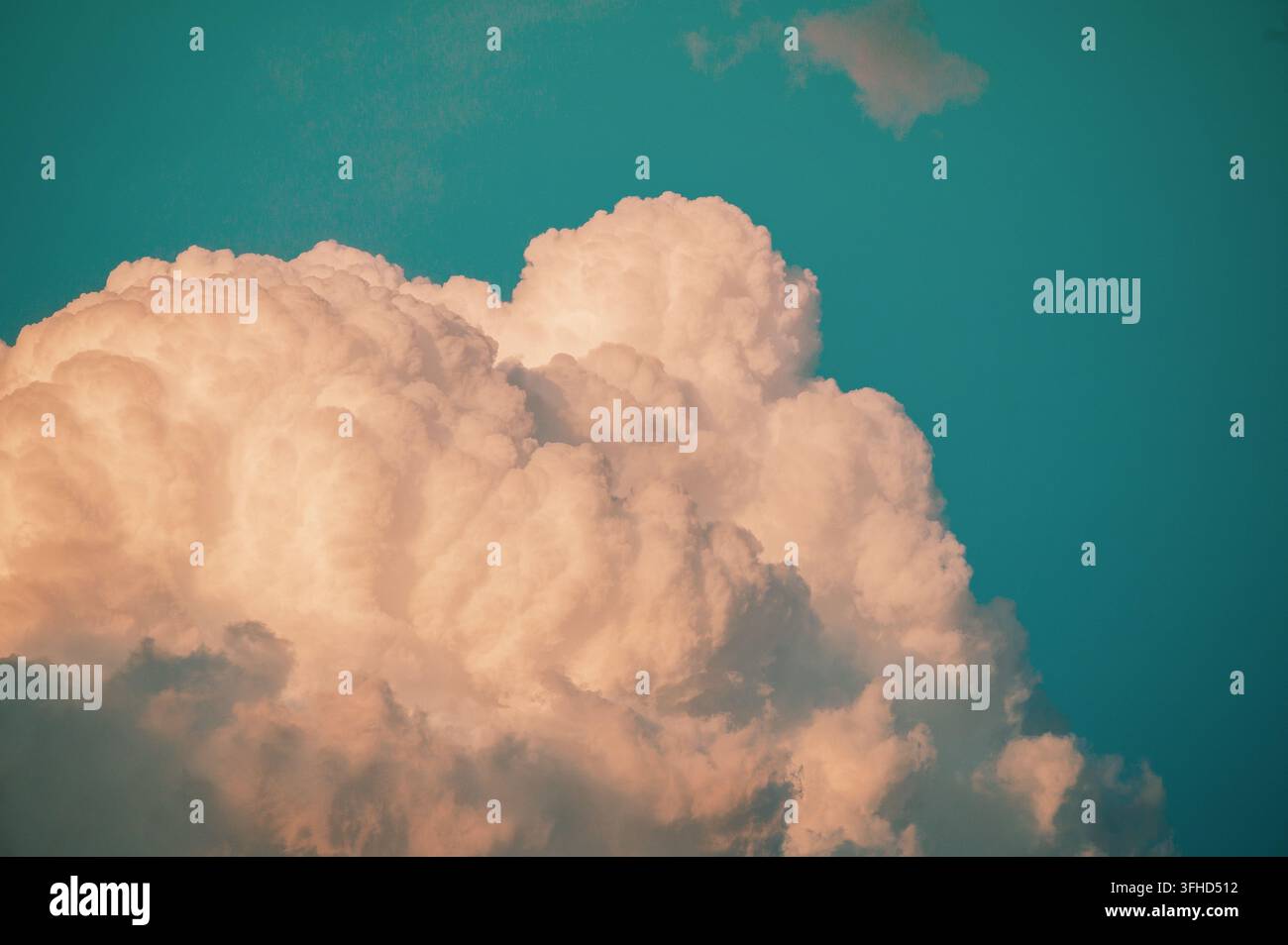 Large fluffy cumulus cloud formation glowing in warm light against a deep blue sky. Stock Photo