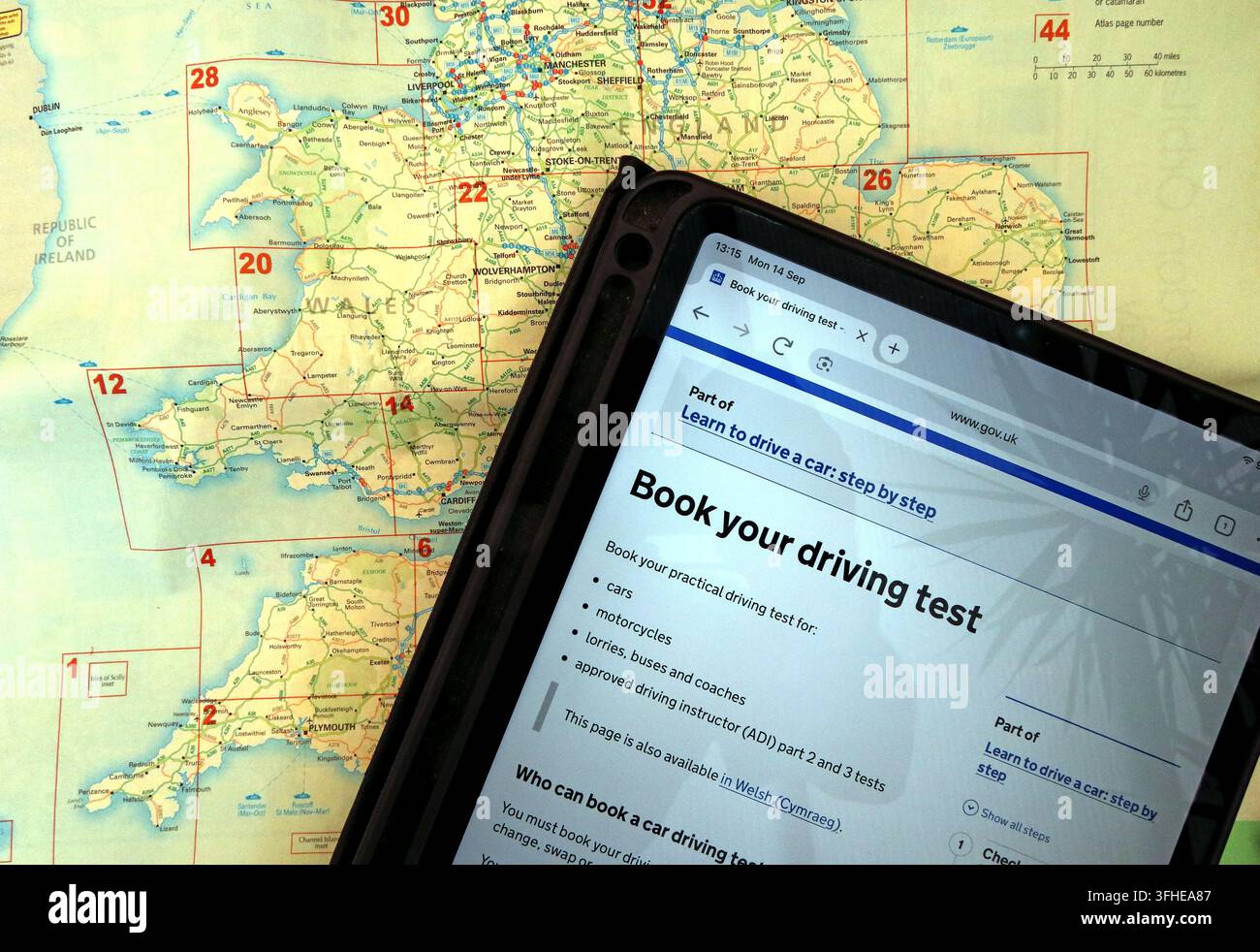GOV.UK driving-test booking page on a tablet over a map of Wales & England amid continuing delays and frustration securing practical test appointments Stock Photo