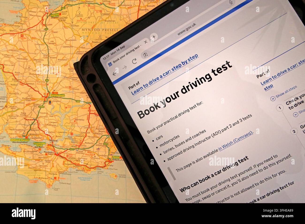 Practical driving-test booking page on GOV.UK displayed on an iPad over a map of Wales, highlighting waiting times facing Welsh learner drivers. Stock Photo