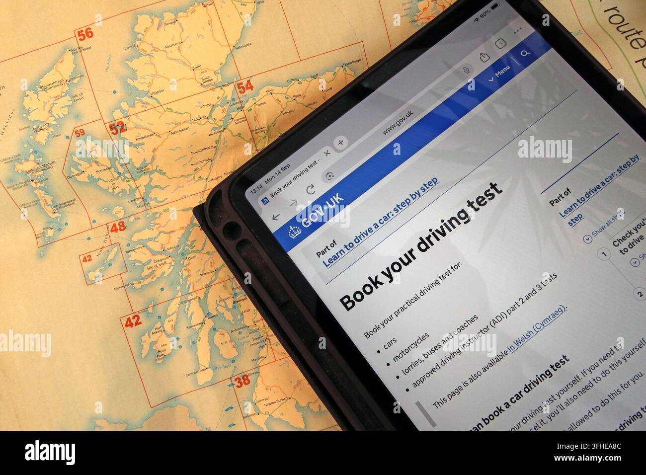 GOV.UK practical driving-test booking page displayed on an iPad over a road map of Scotland, illustrating delays facing new Scottish learner drivers. Stock Photo