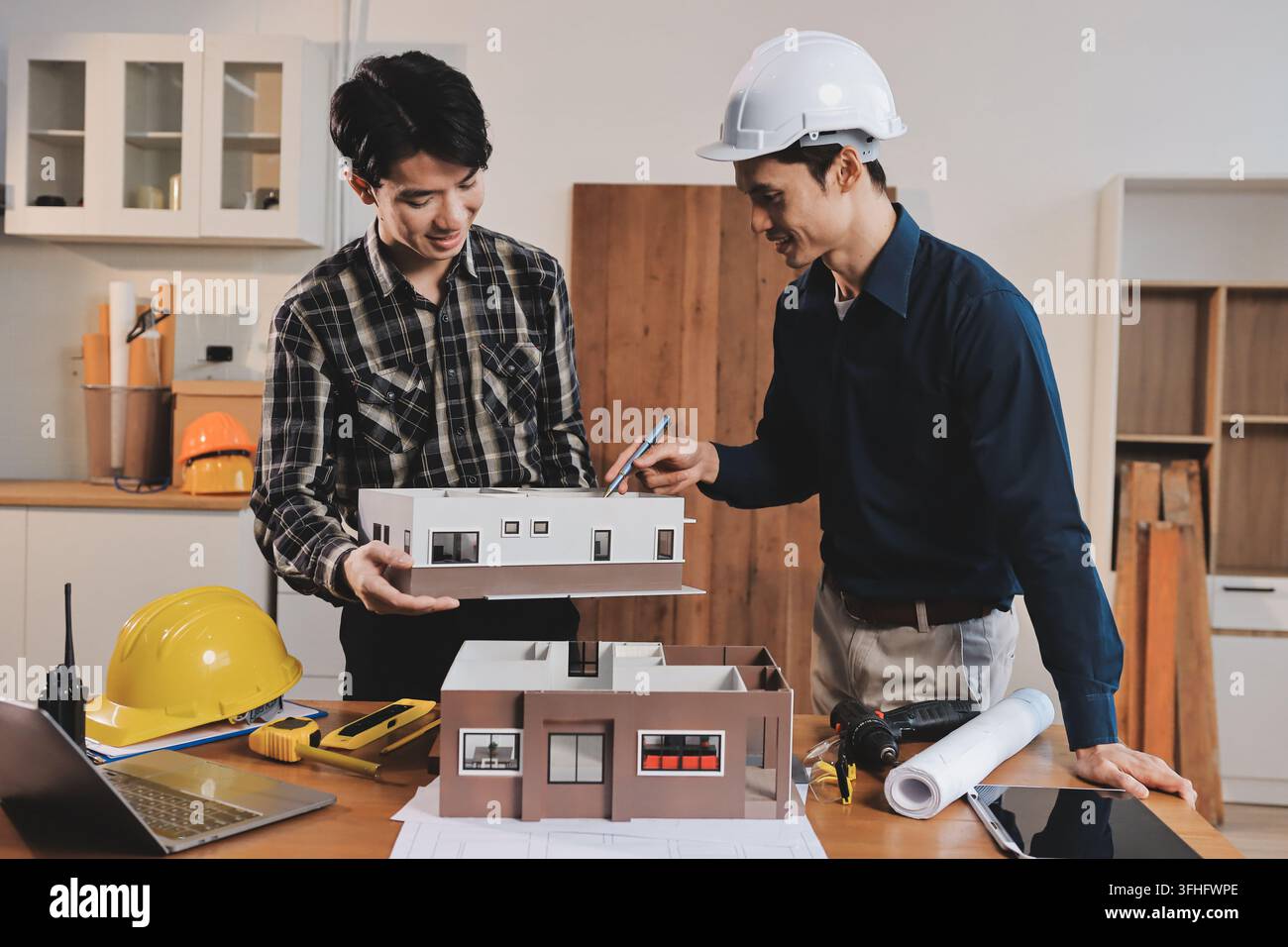 Asian architect and engineer team checking architectural house model using measuring tape on the table at office studio. Stock Photo