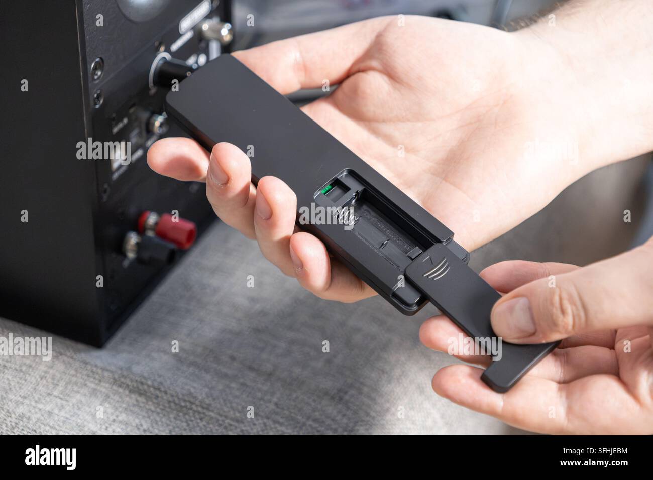 Close up of hands inserting a new power cell into a modern audio device controller, highlighting the essential setup process for maintaining functiona Stock Photo