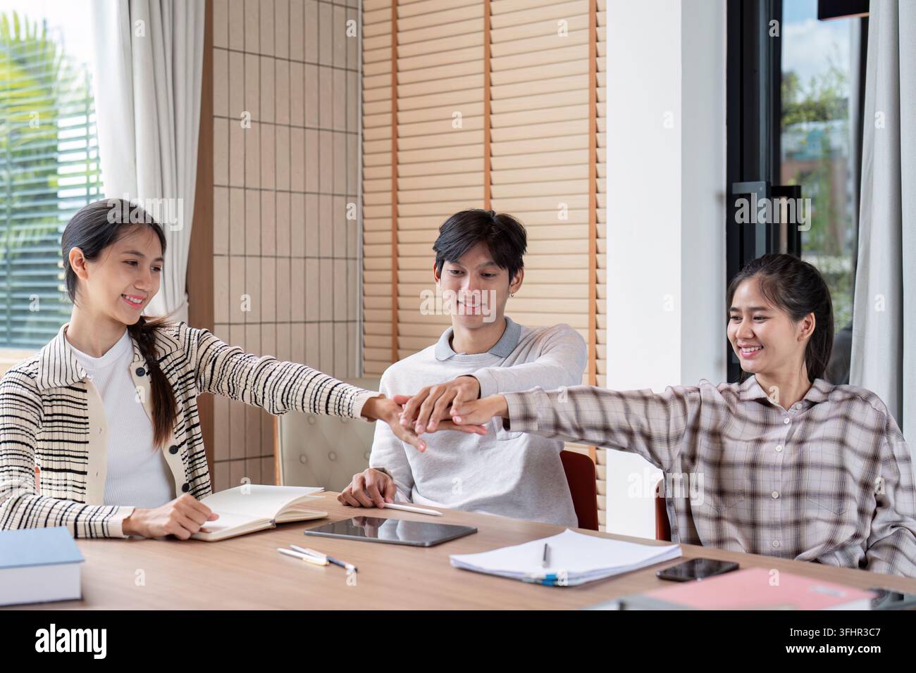 Three students working together, sharing ideas, and studying in a bright, modern classroom environment. Stock Photo