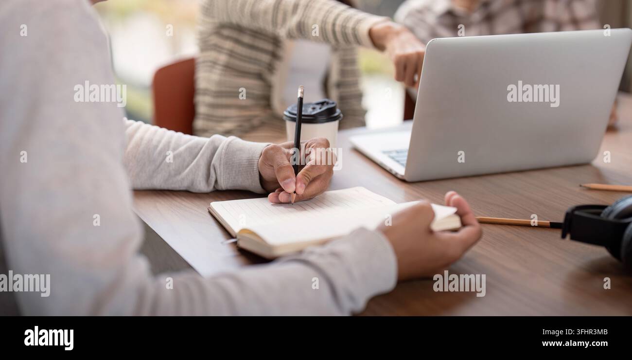 Students engaged in collaborative study session, using laptops and notebooks in a modern classroom environment. Stock Photo