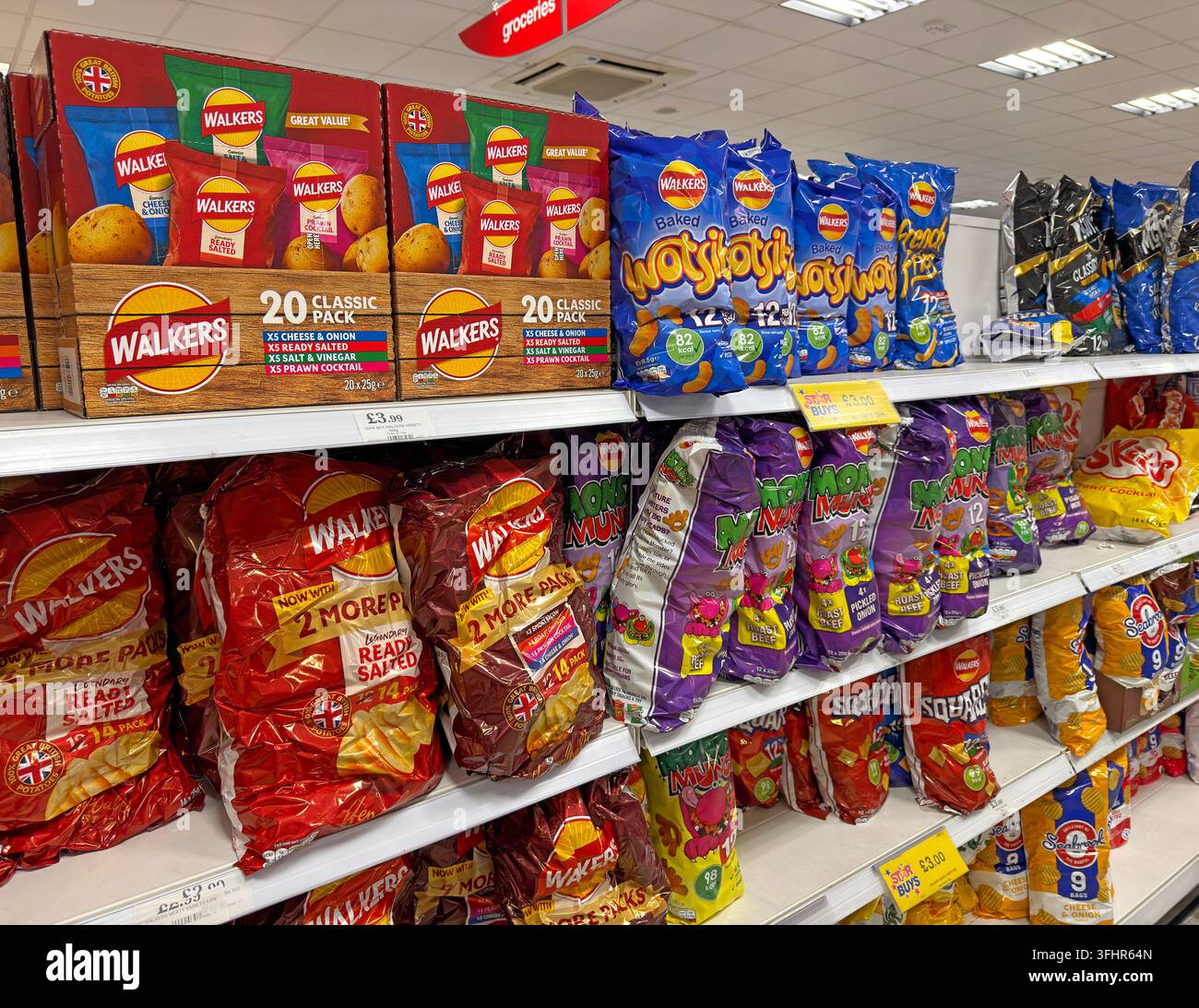 Supermarket snack aisle stocked with Walkers crisps, Wotsits, Monster Munch, Squares and Skips in the UK. Stock Photo