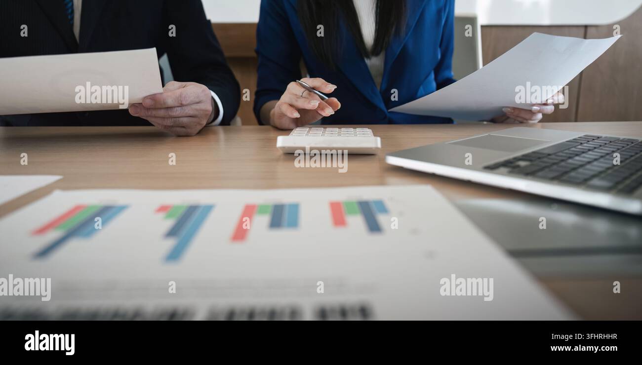 A multicultural business team engaged in analyzing financial documents while using a calculator, highlighting teamwork and analytical focus in a conte Stock Photo