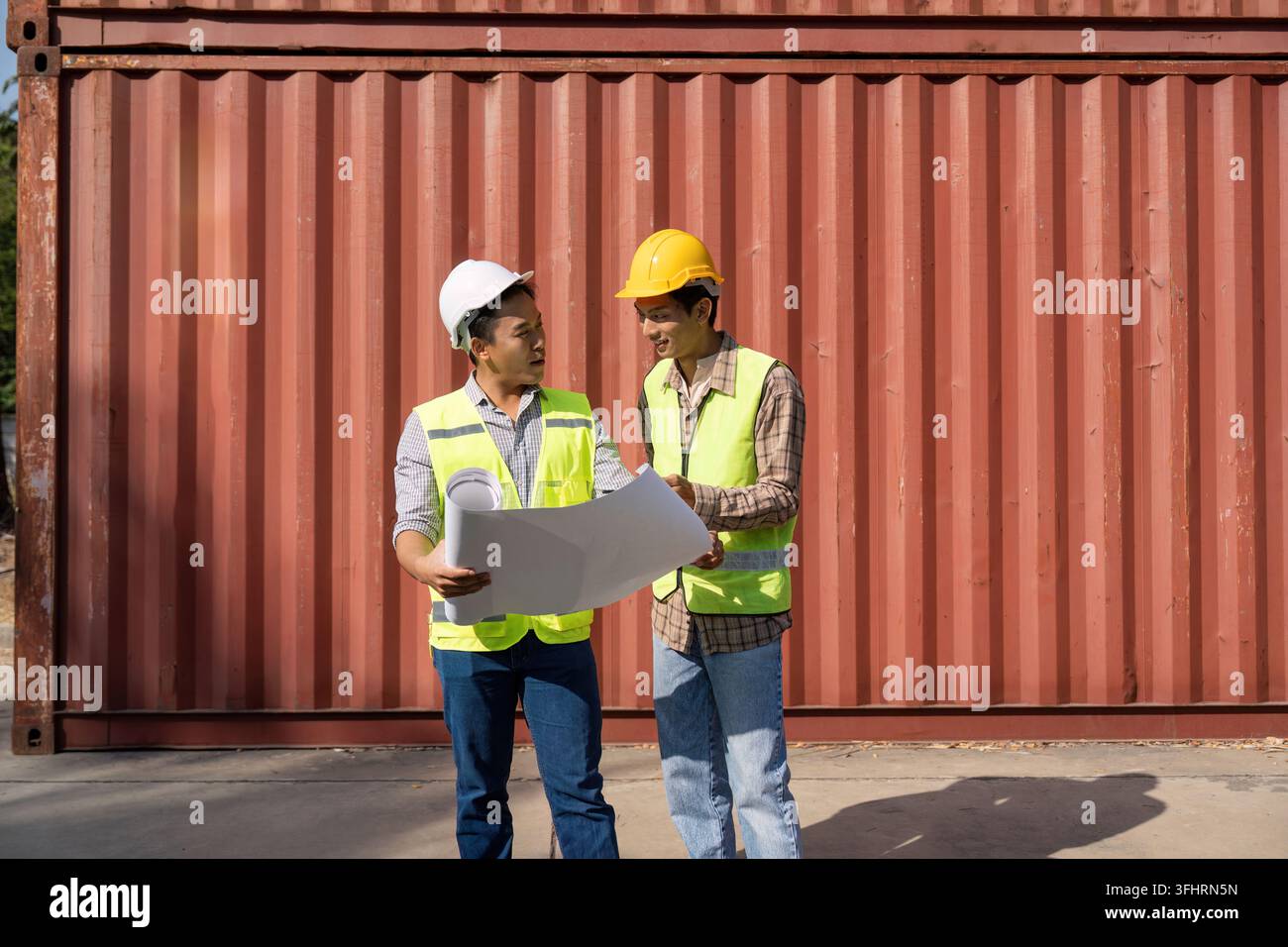 Collaborative Engineering. Two engineers discussing logistics plans in front of shipping containers. Stock Photo