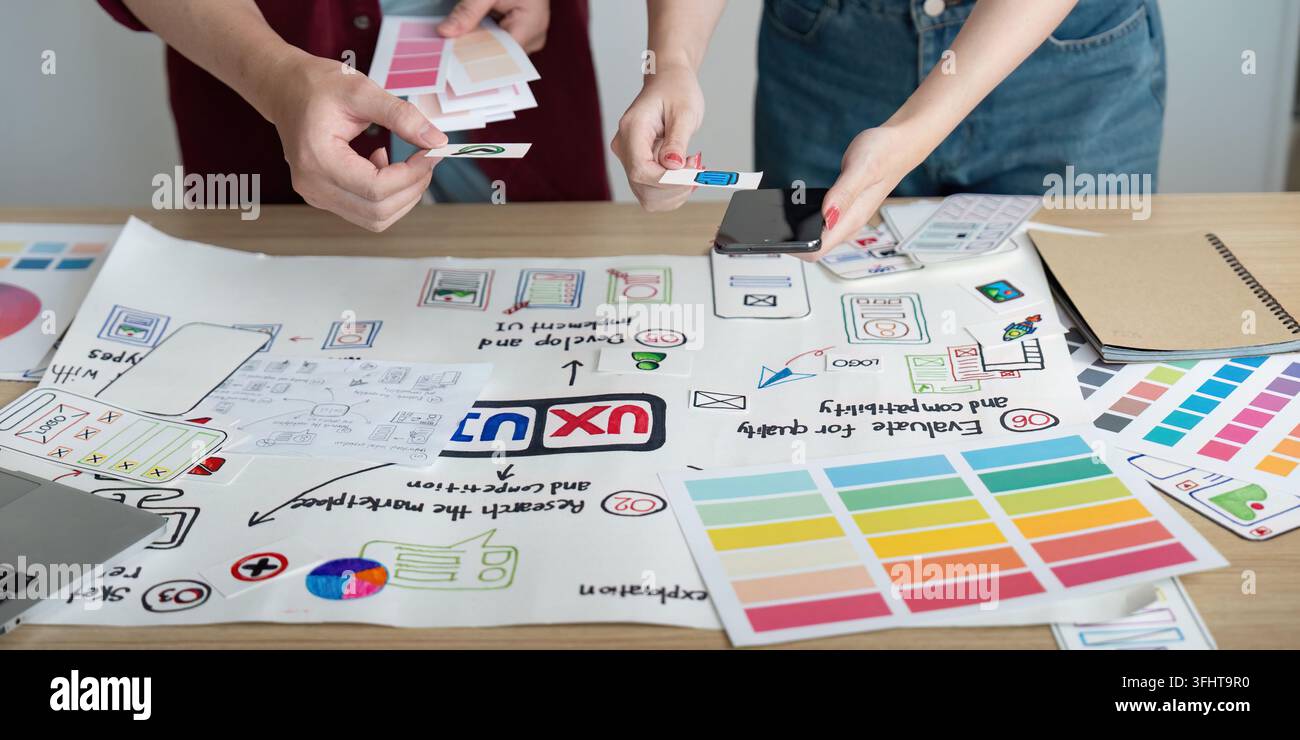 A creative team collaborates on design concepts, sharing ideas and feedback while reviewing project materials on a table. Stock Photo