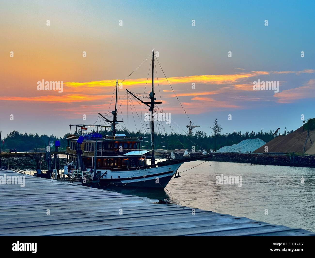 A traditional Indonesian Pinisi boat is moored at a wooden pier against ...