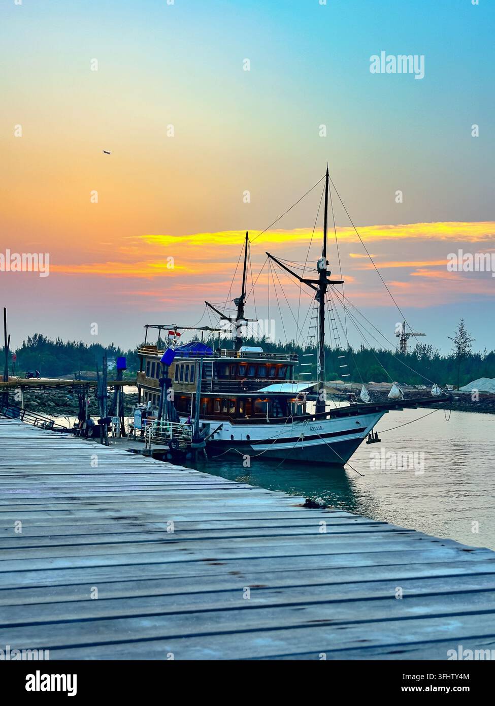 A traditional Indonesian Pinisi boat is moored at a wooden pier against ...