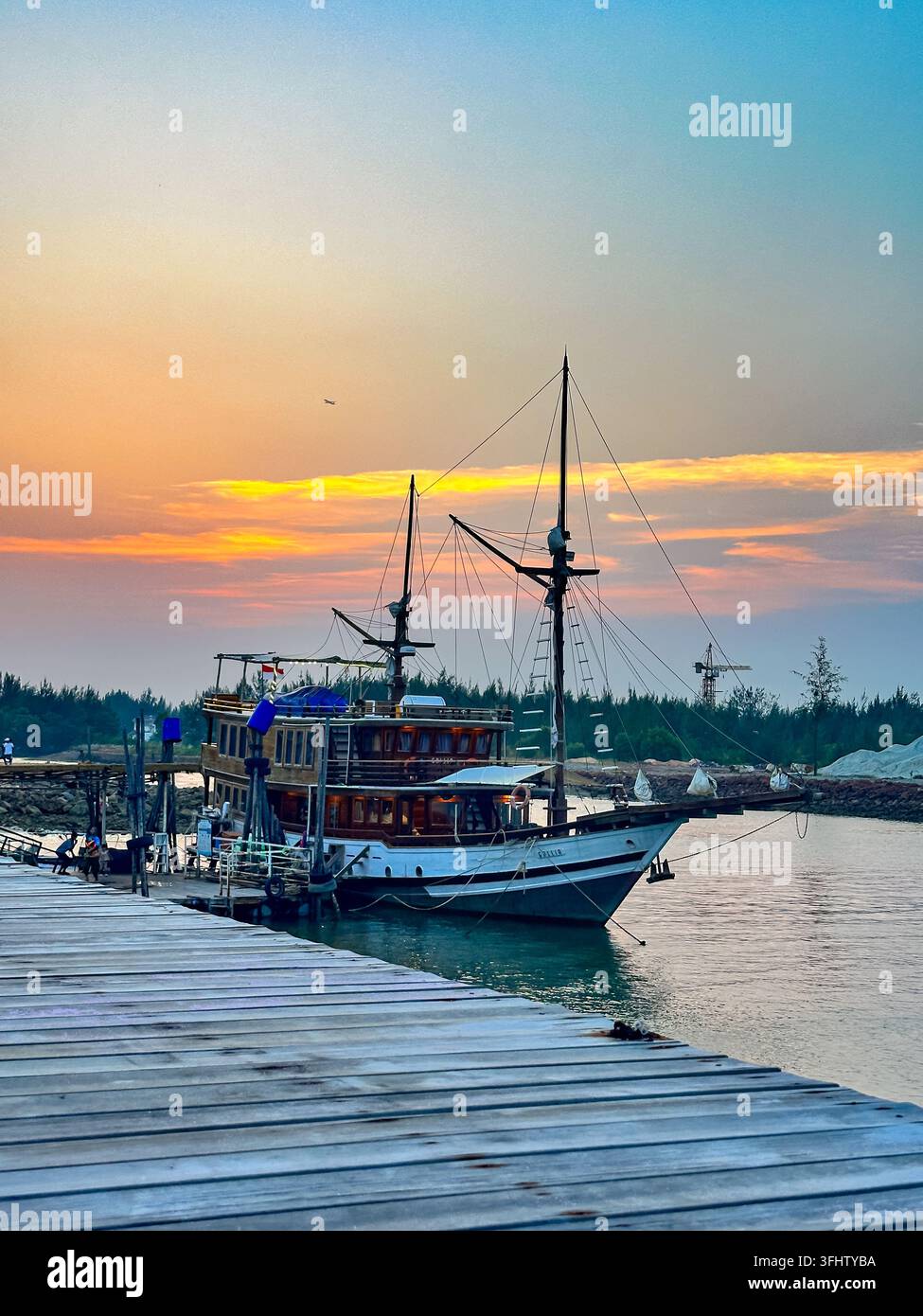 A traditional Indonesian Pinisi boat is moored at a wooden pier against ...