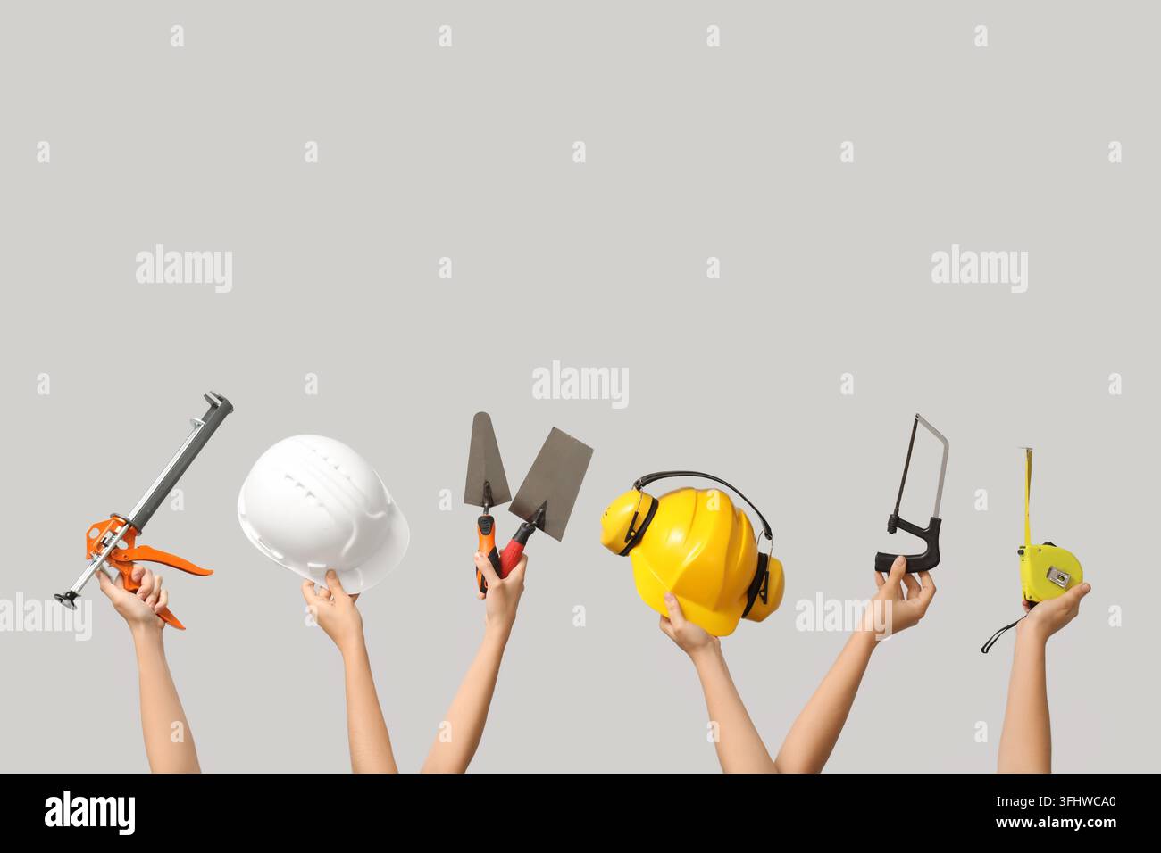 Hands with hardhats and construction tools on grey background Stock Photo