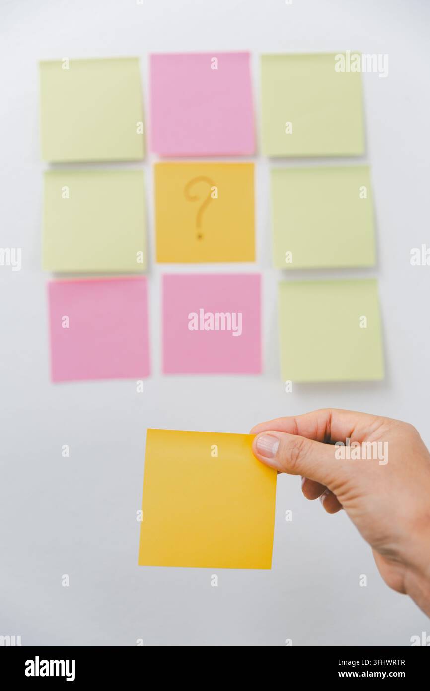 Hand holding a blank yellow sticky note in front of colorful notes with ...