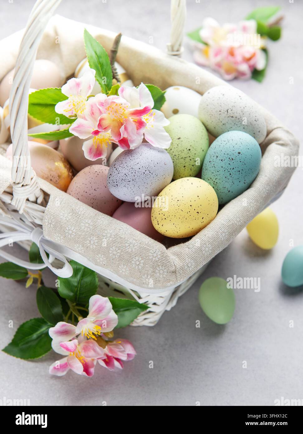 Pastel colored easter eggs overflowing from a white wicker basket decorated with spring flowers Stock Photo