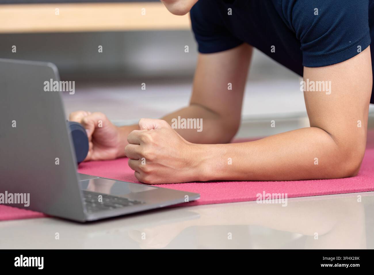 Home Fitness. Young man doing plank exercise with laptop for online workout. Stock Photo