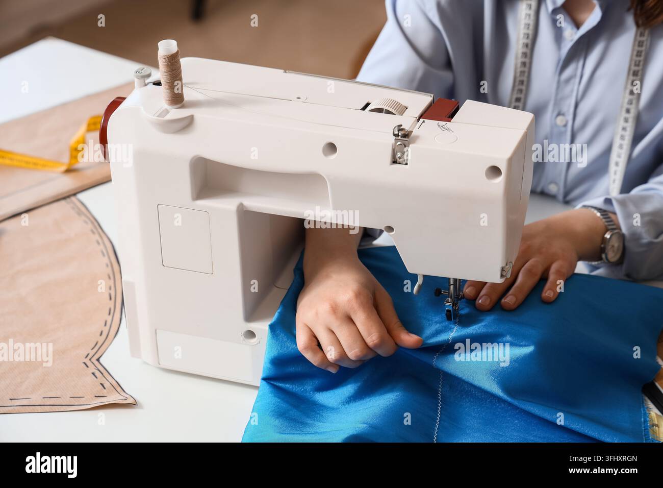 Fashion design and tailoring, dressmaker using a sewing machine to stitch blue fabric with pattern paper and measuring tape in a creative workshop Stock Photo