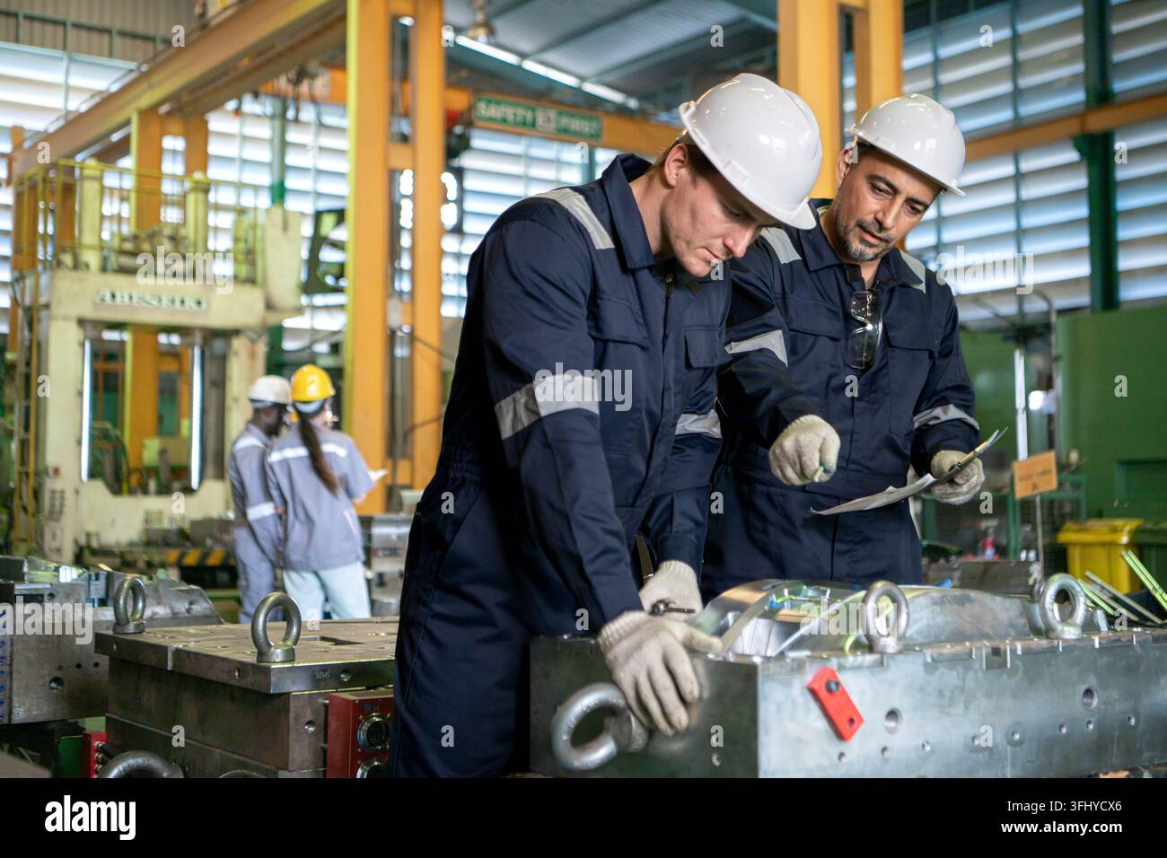 Industrial engineers and technicians discussing machine operation while inspecting equipment in a manufacturing factory Stock Photo
