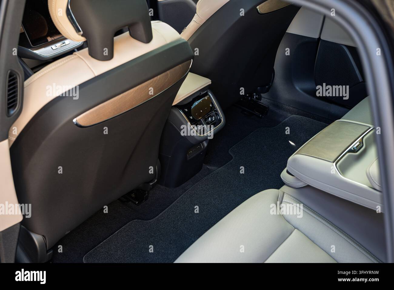 View into the rear seating area of a modern luxury car showing light beige leather seats, generous legroom, floor carpet, and rear climate control uni Stock Photo