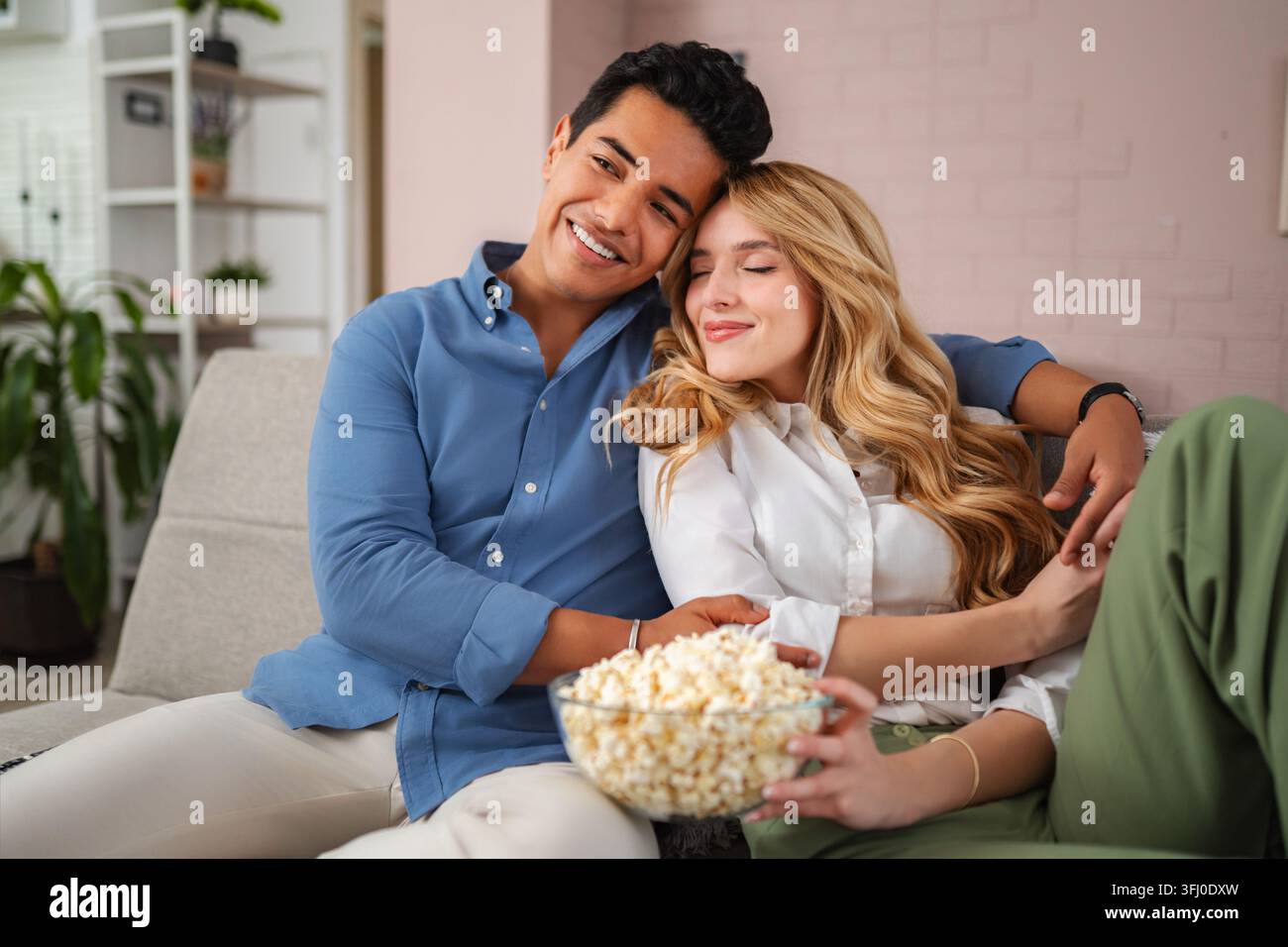 Happy young couple relaxing on sofa watching movie eating popcorn Stock Photo