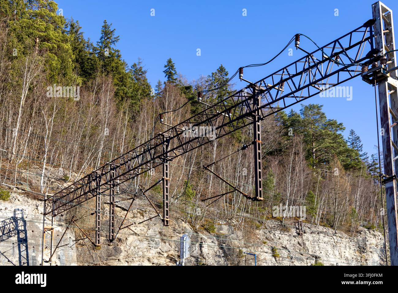 Metal catenary structures support electrical cables above a railway track near a rocky slope, symbolizing engineering precision and connectivity in pu Stock Photo