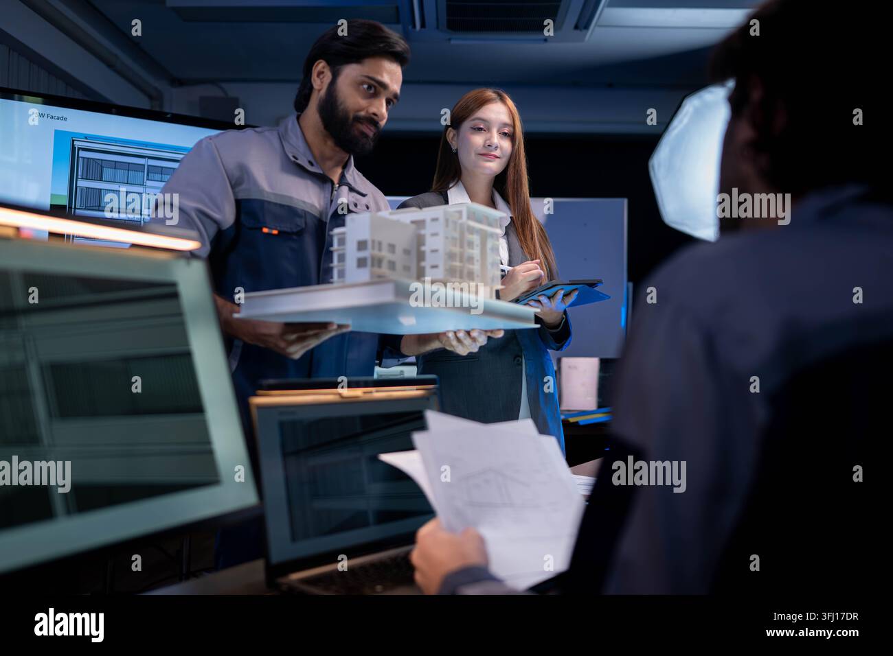 Engineering and business professionals discussing architectural building model and project development strategy in modern collaborative workspace Stock Photo