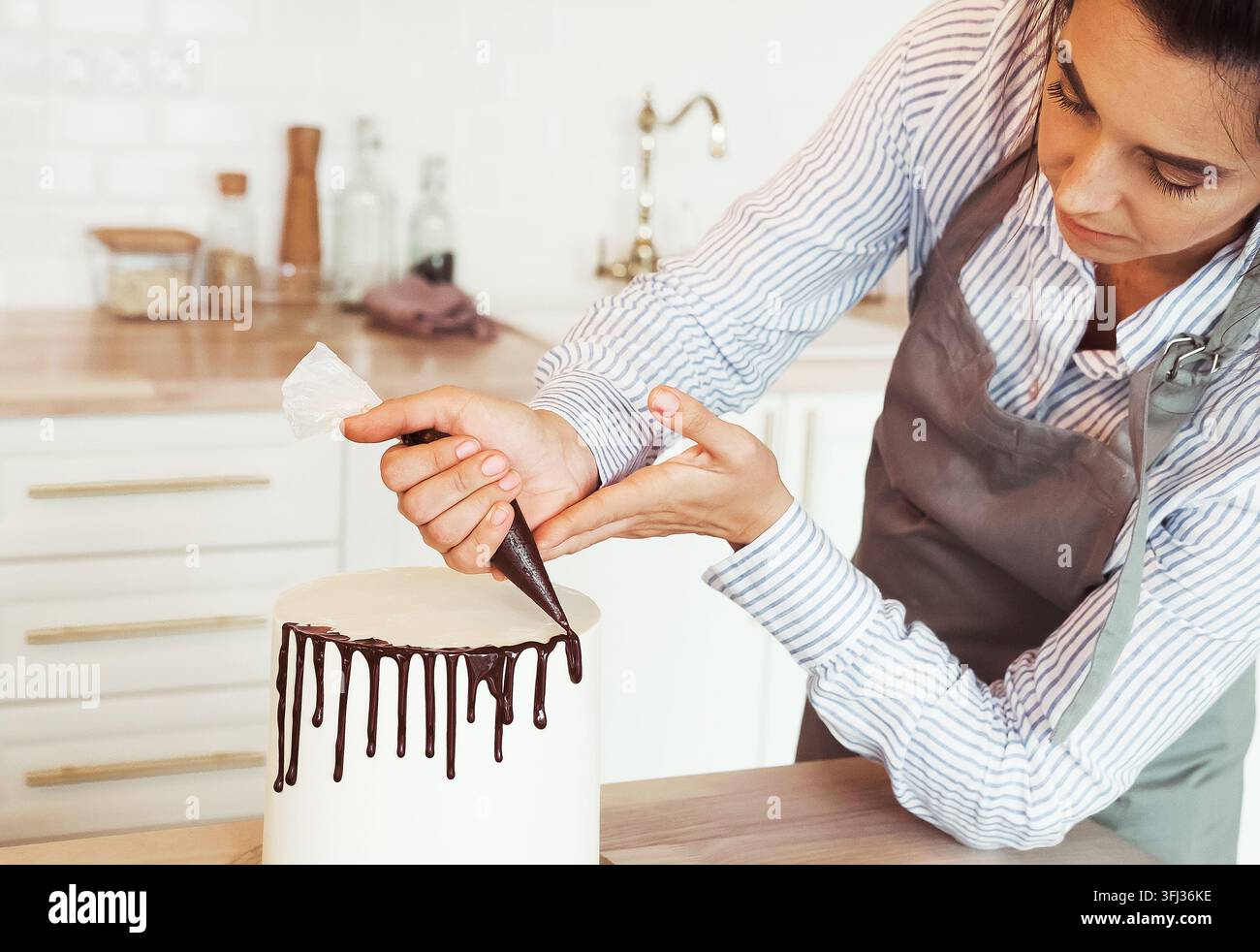 Pastry female chef in the kitchen decorating a cake of chocolate. Stock Photo